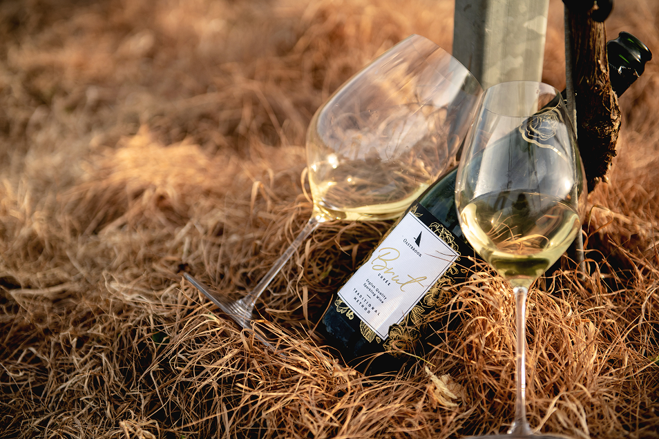 Two wine glasses and a bottle of white wine resting on a straw-covered ground at Oastbrook Vineyard