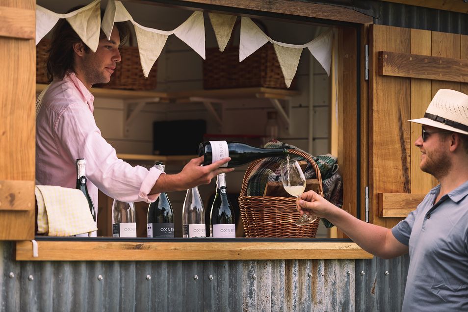 A person serving wine to a visitor at the outdoor tasting bar at Oxney Organic Estate