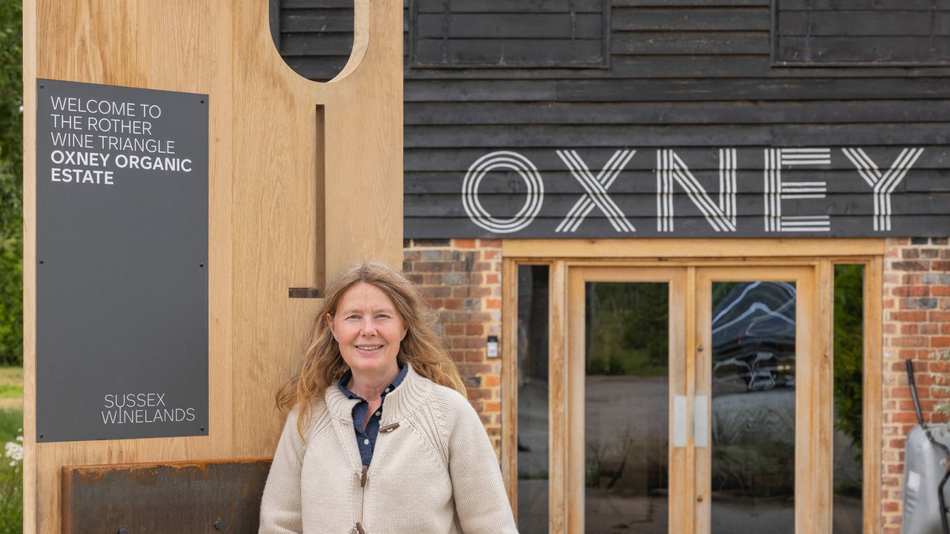 The vineyard owner stood infront of the Sussex Winelands signage installed at Oxney Organic Estate