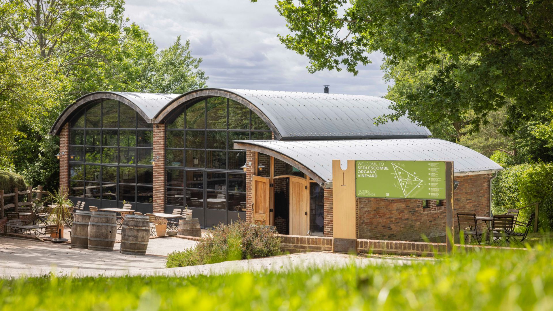 A view of Sedlescombe Organic Vineyard and outdoor seating framed by trees with the Sussex Winelands signage in the foreground